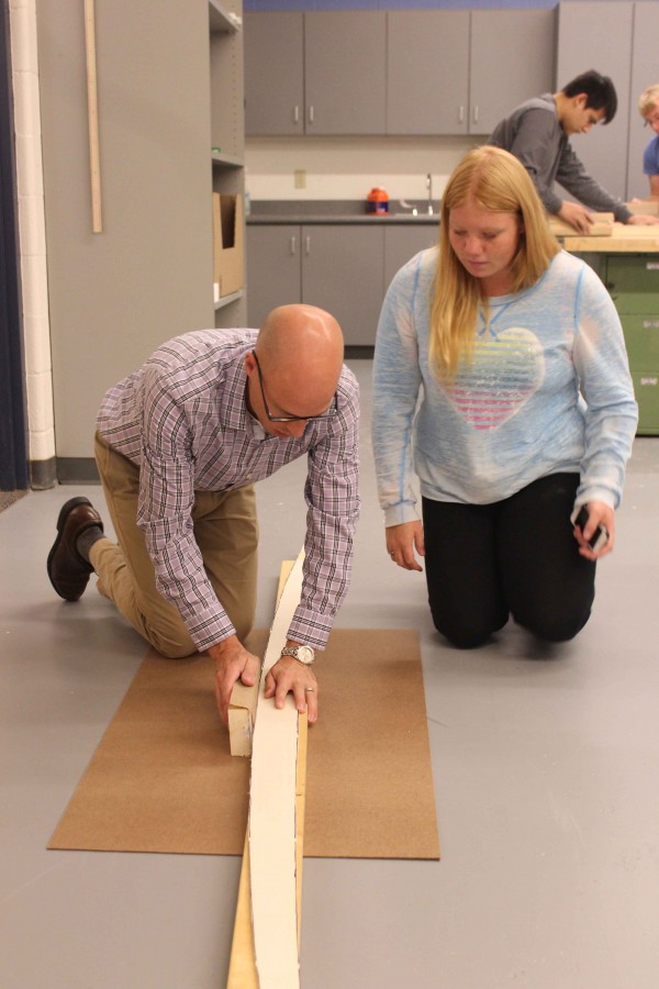 Senior Ashley F watches technical education teacher Jeremy Case demonstrate construction of her surfboard. An auction will be held in May.