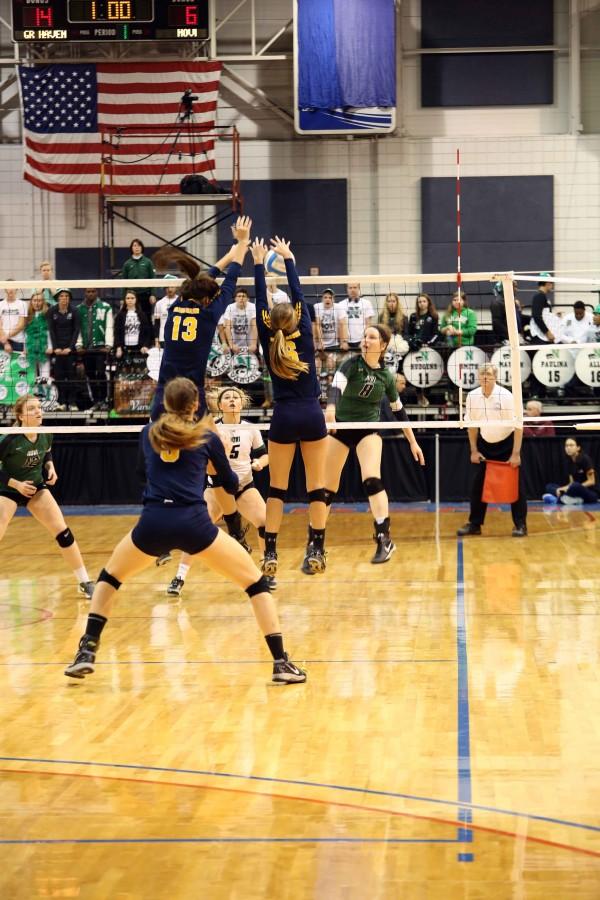 Players Ally Knoll and Katie Cole go up for a block agains a Novi outside hitter. Senior Amy Kober covers from behind watching for a hole in the block ready to pick up anything that comes her way. 