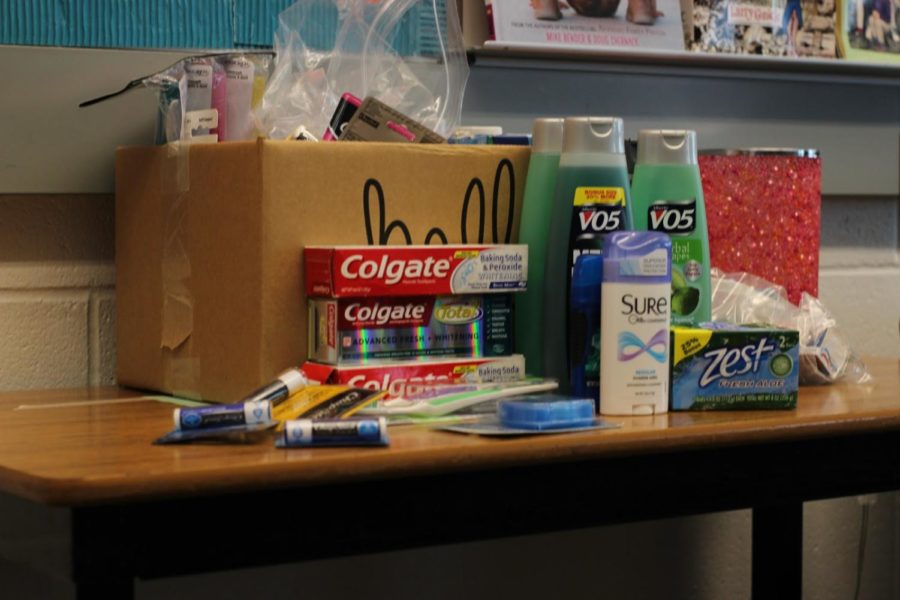 A bundle of toothpastes, soaps, shampoos, and more rest on a desk.