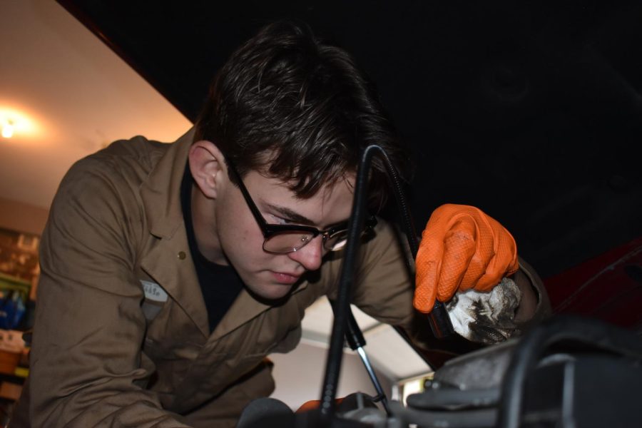 HARD AT WORK: Senior Rob Tayler shines a flashlight on the engine as he cleans the oil gasket material. Cleaning is essential before putting the engine back together.