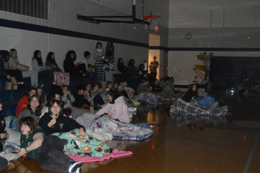 Students sit on bleachers and blankets in the Aux gym to watch Monsters Inc.